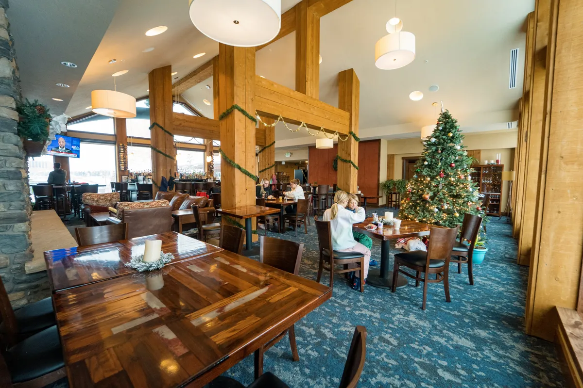 A vibrant, communal interior lounge area with large wooden beams, a cozy seating arrangement, a festive atmosphere, and a visible bar area. This space is ideal for dining, socializing, and celebrating with friends and family.