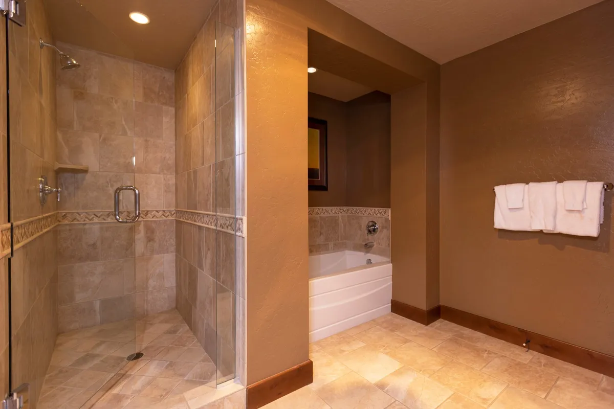 A luxurious bathroom with a glass-enclosed shower, elegant bathtub, decorative tile trim, and a wall-mounted mirror. The overall atmosphere is tranquil and spa-like, ideal for soaking or a refreshing shower.